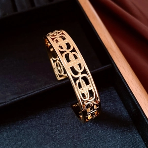 Detailed shot of an 18K gold-plated open bangle with cutout patterns in a black box