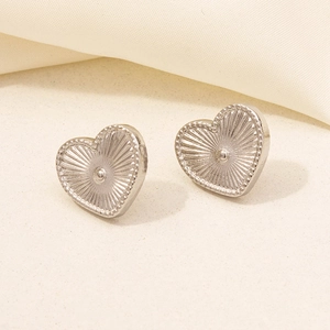 Macro shot of silver heart studs with radial texture and metallic finish on soft fabric