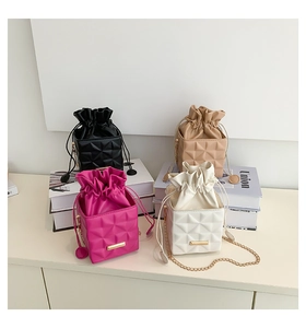 Close-up of quilted bucket bags in four colors with gold chain straps on a white desk