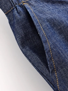 Macro view of indigo denim shirt pocket featuring yellow double-stitch high-density seams