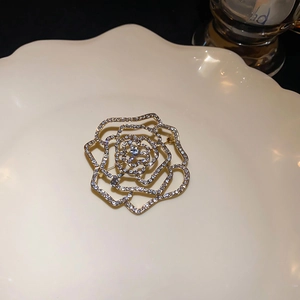 Detail of 18k gold plated rose brooch featuring cubic zirconia inlay on a ceramic plate