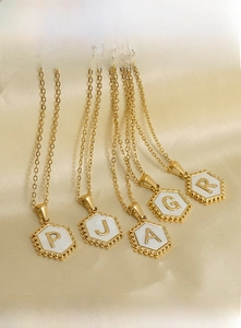 Detail of 18K gold stainless steel hexagonal necklaces with white enamel letter pendants