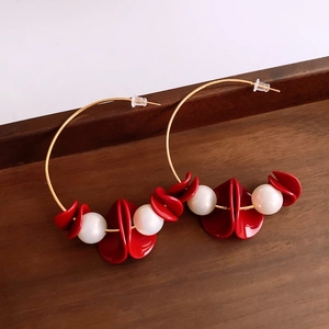 Detail of gold hoop earrings featuring red petal accents and white pearls on wood