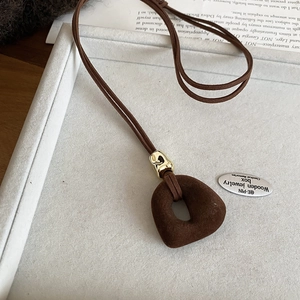 Macro detail of brown flocked pendant and golden metal connector on a velvet cord necklace