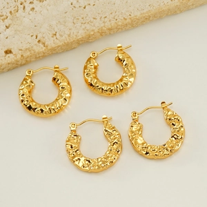 Detailed close-up of golden U-shaped earrings with hammered texture on a beige stone surface