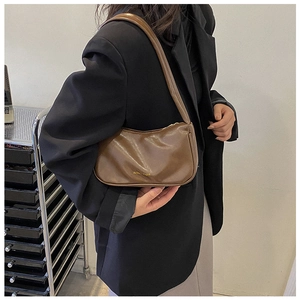 Detail of a brown leather baguette bag with gold FASHION BAG text on a black blazer