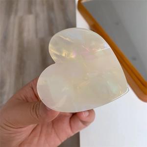 Detail of heart-shaped hair claw clip with pearlescent white finish and iridescent luster