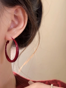 Macro side view of a model wearing large smooth deep red glazed hoop earrings
