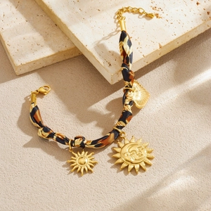 Leopard print fabric chain bracelet with gold sun and heart charms on a stone background