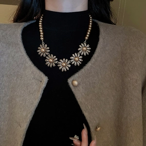 Close-up of golden pearl necklace with crystal flower pendant worn on a model