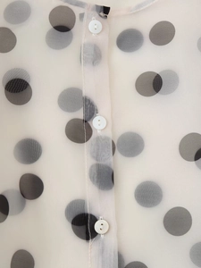 Detail shot of sheer organza fabric with black polka dots and white buttons on the placket
