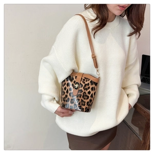 Model wearing leopard print bucket bag with brown leather accents and adjustable strap