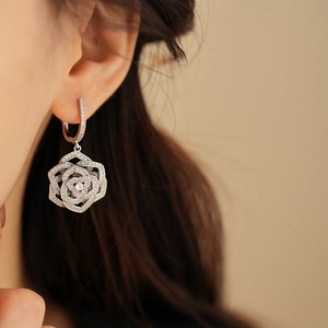 Close-up of silver hollow flower zircon earrings worn by a model in soft lighting