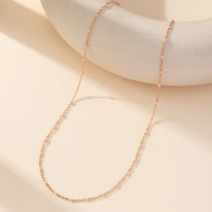Minimalist gold link necklace with pink enamel bead accents on a cream geometric stand