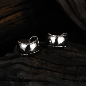 Polished silver wide-surface ear clips with beaded edge on dark wood background