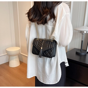 Close-up of quilted black leather bag with gold chain strap and tassel detail
