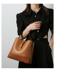 Detail view of brown textured leather handbag featuring golden metal buckle and gold base studs