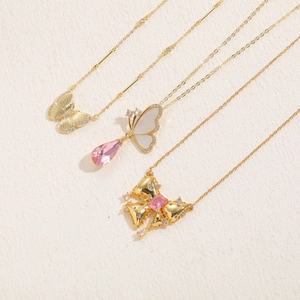 Macro shot of three gold necklaces with pink butterfly and zircon crystal pendants