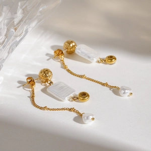 Elegant gold earrings with baroque pearls and square shell pendants on a textured surface