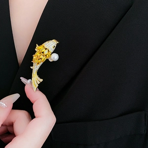 Dettaglio della spilla a forma di carpa koi con pietre gialle e perla su un blazer nero