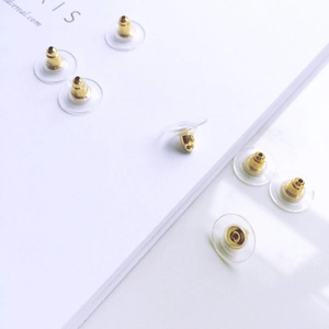 Close-up of clear silicone earring backings with gold metal clips on a white book