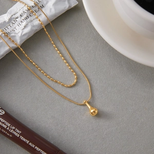 Detailed view of double-layered gold snake chain and bead necklace with water drop pendant