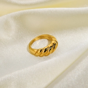 Close-up of golden 18K gold plated croissant ring on soft cream silk fabric background