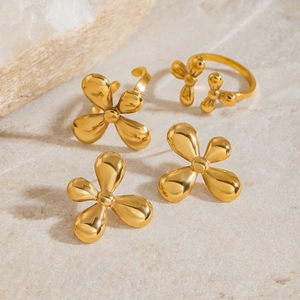 Macro shot of gold-plated four-leaf clover earrings and ring on a marble stone surface