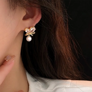 Élégantes boucles d'oreilles nœud dorées avec strass brillants et perle blanche pendante