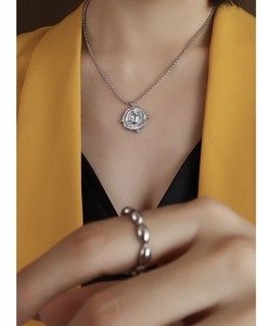 Detail of silver ball chain necklace with round coin pendant on a yellow suit blazer