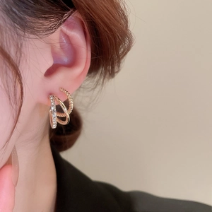 Detail of layered gold C-shape earrings with twisted texture and crystal rhinestones