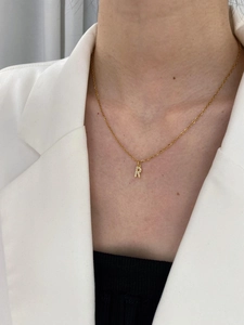 Close-up of a gold chain necklace with a sparkling pavé letter R pendant on a model