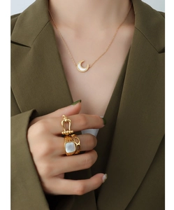 Detail shot of moon-shaped shell necklace and chunky gold-plated rings on model