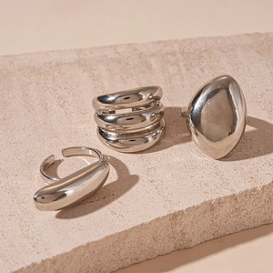 Detailed view of three minimalist silver geometric rings on a beige stone surface