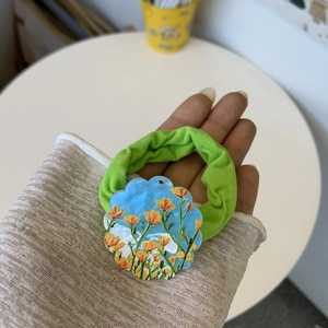 Detail of floral sunflower acrylic charm on green elastic scrunchie being held