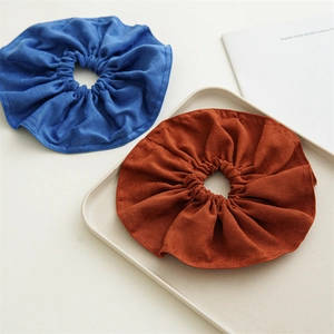 Close-up of oversized suede scrunchies in blue and caramel on a minimalist tray
