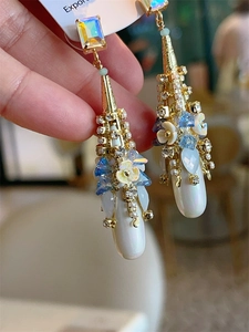 Detail of bohemian drop earrings with gold metal, white pearls and blue crystals