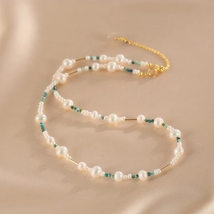 Detail of layered natural pearl and turquoise necklace with gold accents on silk