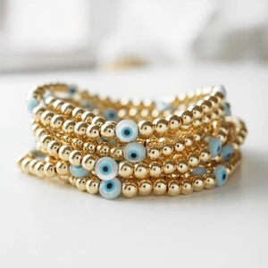 Macro detail of elastic evil eye beaded bracelets with polished 18K gold-plated metal beads