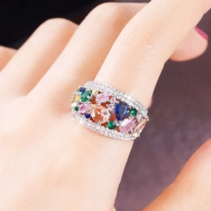 Close-up of a wide silver ring with colorful pear-cut gemstones and sparkling micro-pave