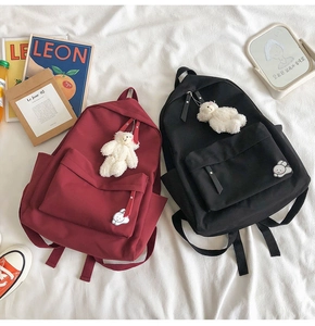 Flat lay of nylon student backpacks in burgundy and black with plush bear charms