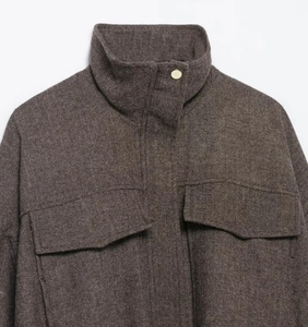 Detailed macro view of dark brown herringbone bomber jacket with golden metal button closure