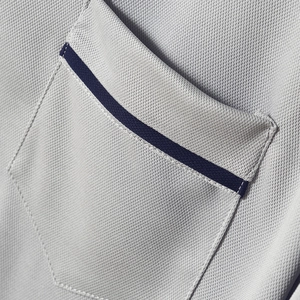Makroaufnahme der Brusttasche eines Poloshirts mit marineblauer Borte auf grauem Piqué-Stoff