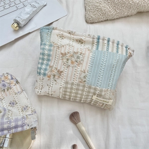 Quilted floral makeup bag detail showing lace weave, metal zipper and brand label