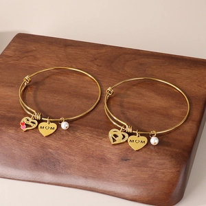 Detail of adjustable gold MOM bracelets with heart pendants and white pearls on wood