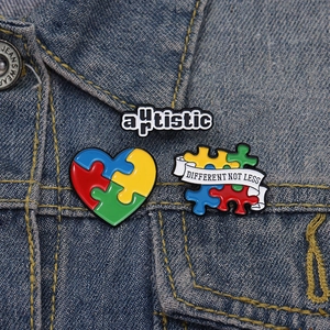 Three autism awareness puzzle pins and badges displayed on a blue denim jacket pocket