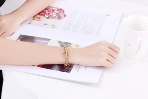 Dettaglio del bracciale dorato a doppio strato con cuore al polso con eleganti accessori
