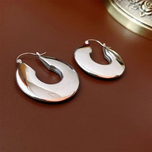 Detailed view of polished silver U-shape hoop earrings on premium brown leather texture