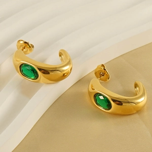 Golden C-shaped stainless steel earrings with emerald zircon stones on beige background