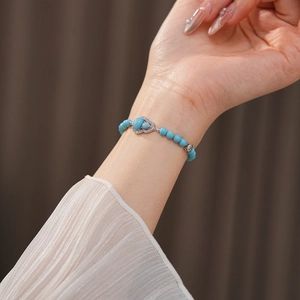 Close-up of beaded turquoise bracelet with heart-shaped pendant on woman's wrist